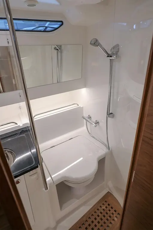 Compact bathroom featuring a shower, toilet, mirror, and sink with a wood slatted floor and modern fixtures.